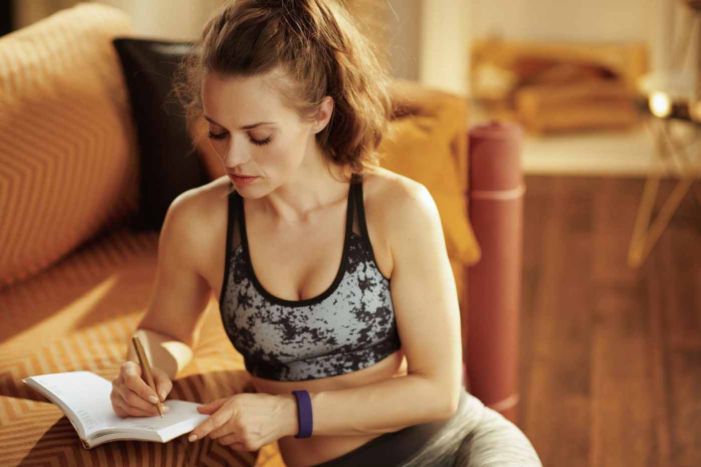 young woman in athletic attire with journal and pen writing goals and training log 