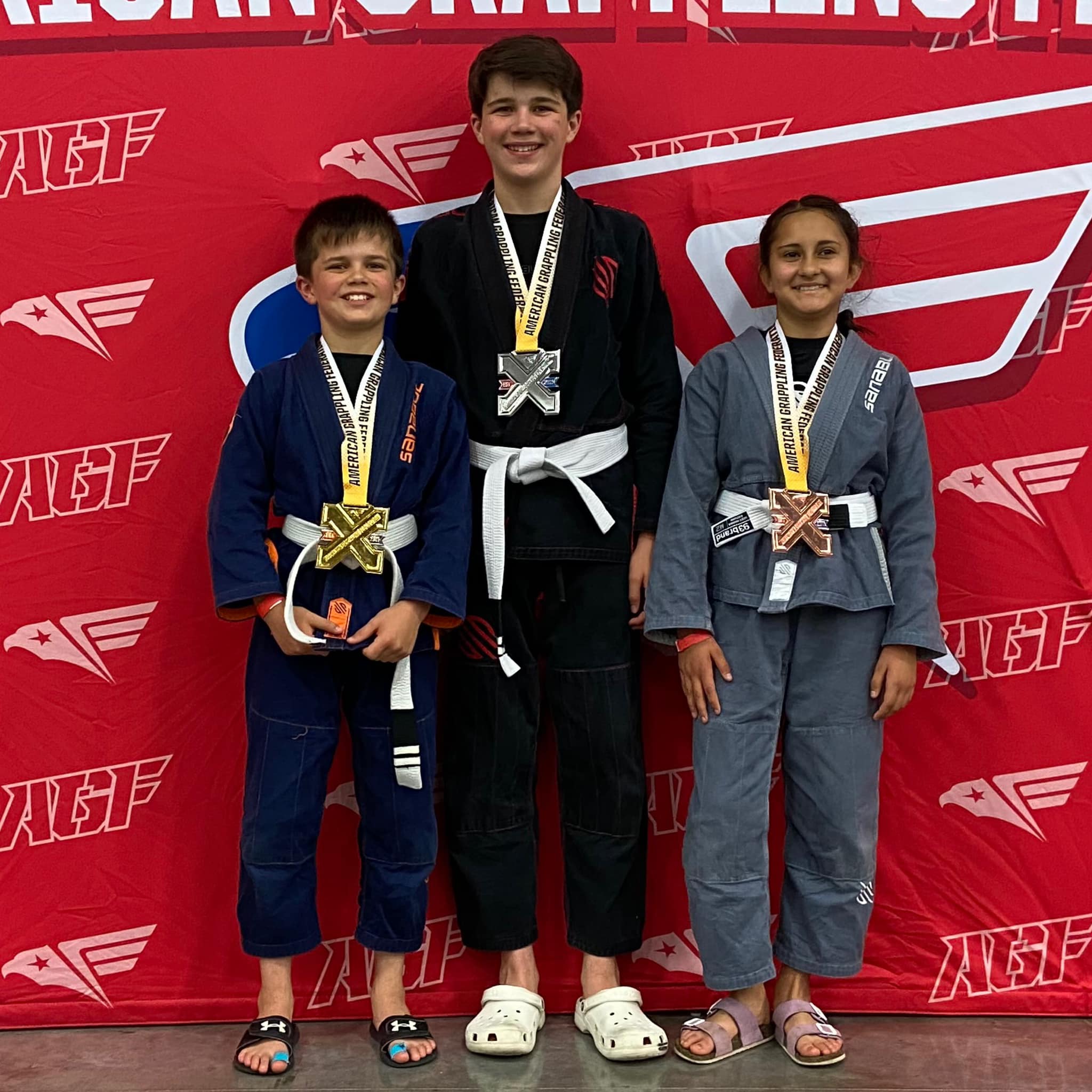 Three children receiving their medals after a Brazilian Jiu Jitsu competition