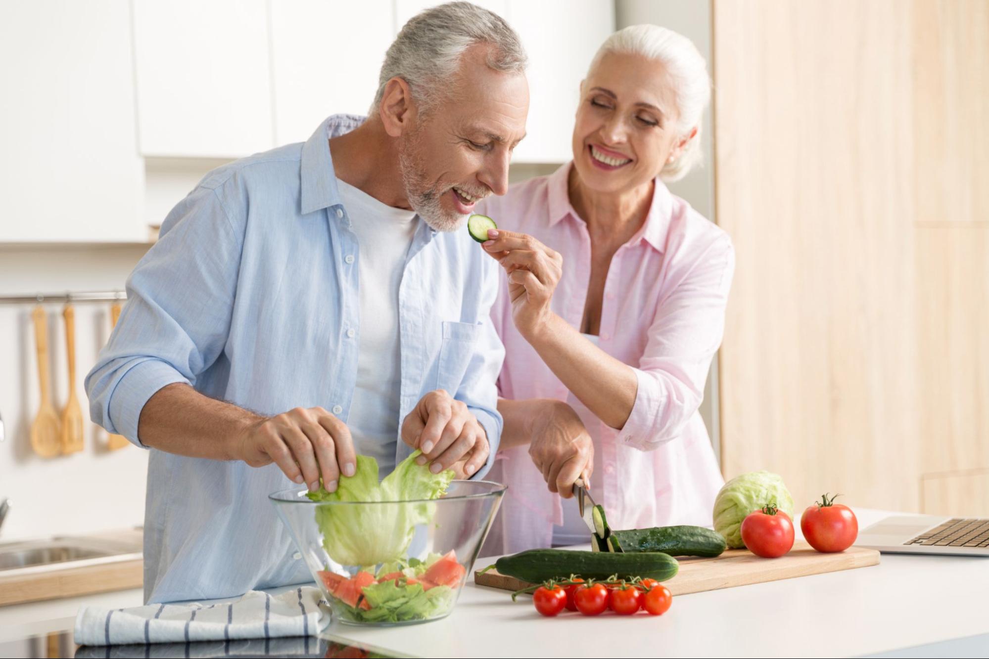 Mature couple having fun in their kitchen making a salad together