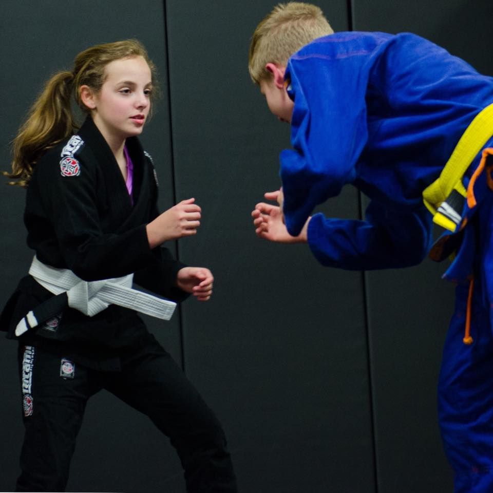 Young girl in a black gi sparring with another student wearing a blue gi