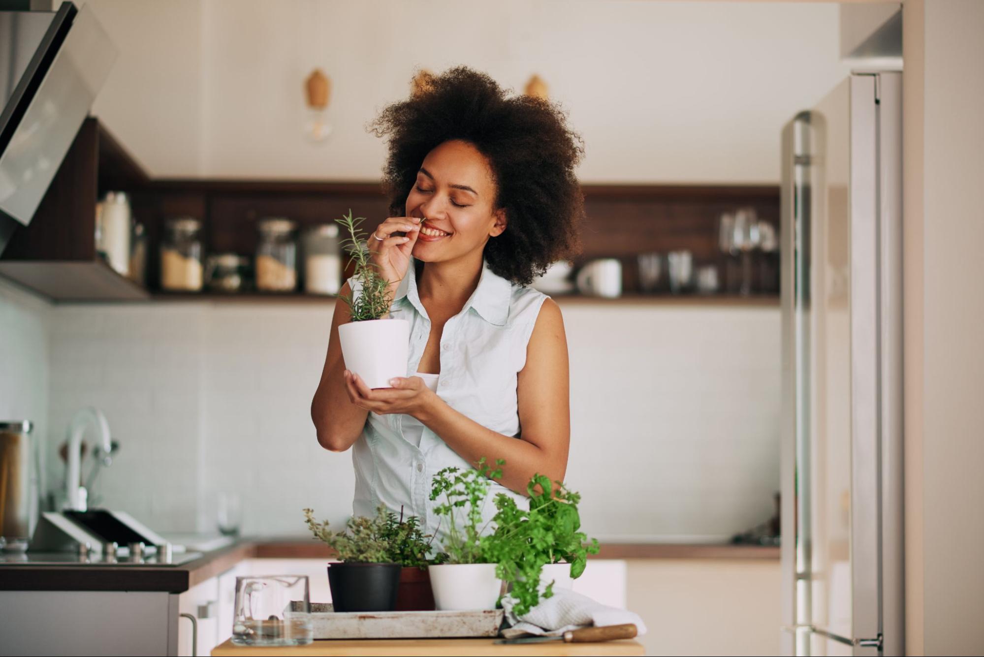 Young woman smells fresh herbs she grows in her kitchen to use when flavoring her dishes