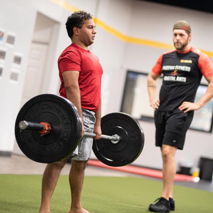PFMA personal trainer looking on as an athlete lifts a heavy barbell