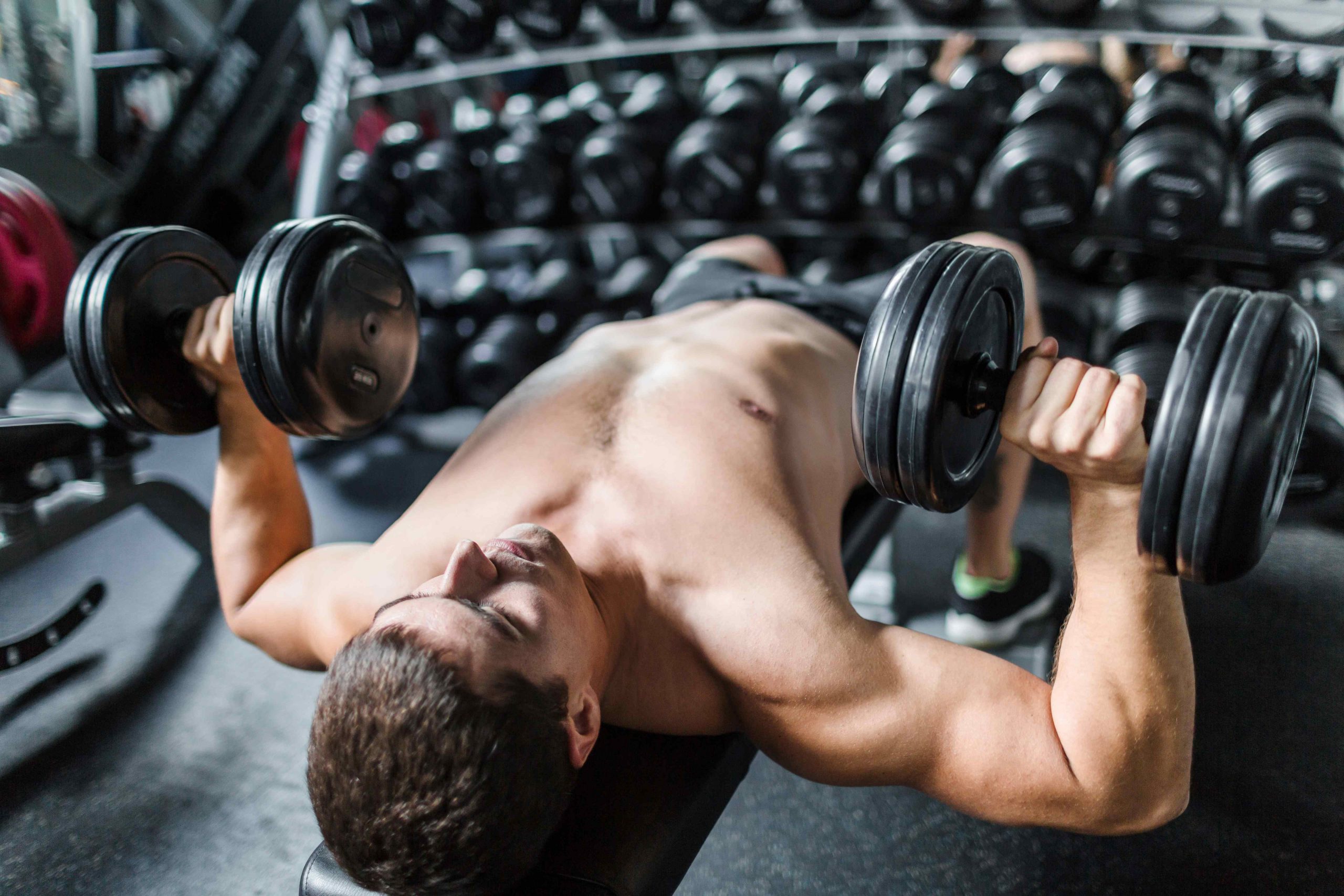 Man lays on exercise bench holding 2 dumbbells for strength training
