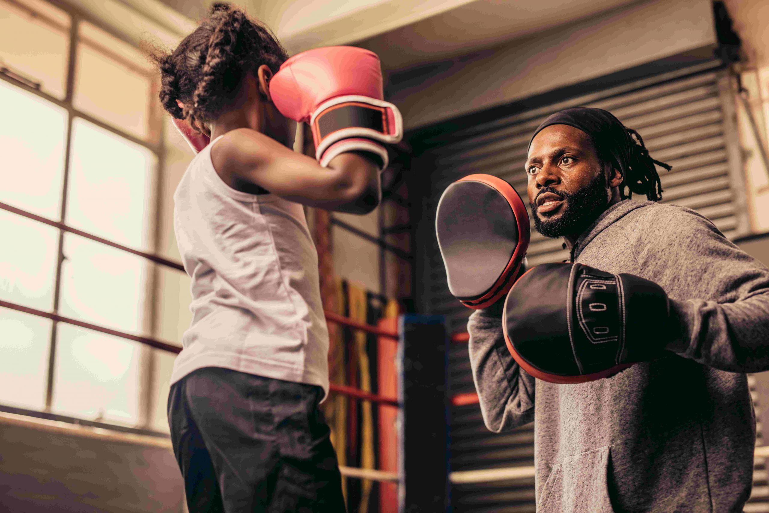 Young child practicing punches with a coach wearing boxing gloves