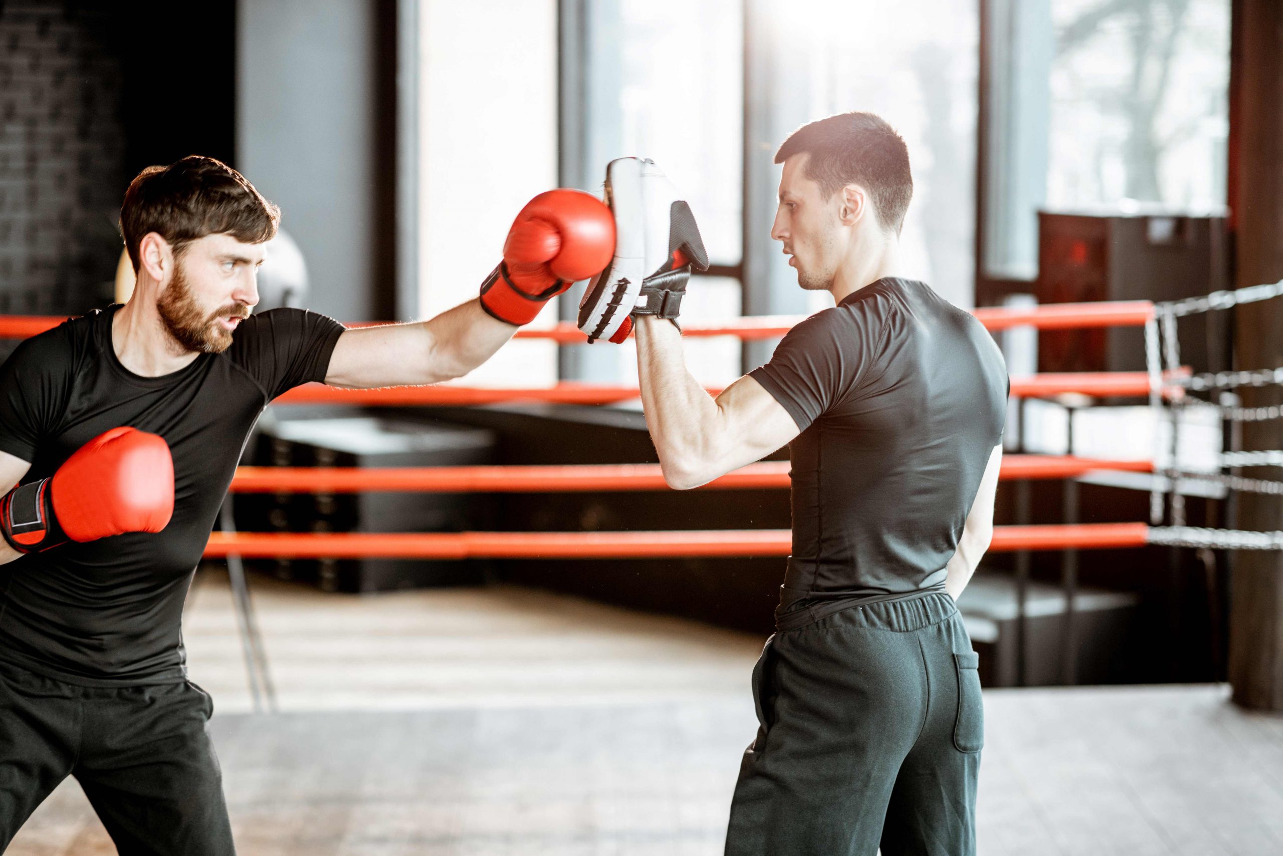 Athletic man training with boxing trainer in the boxing ring at the gym