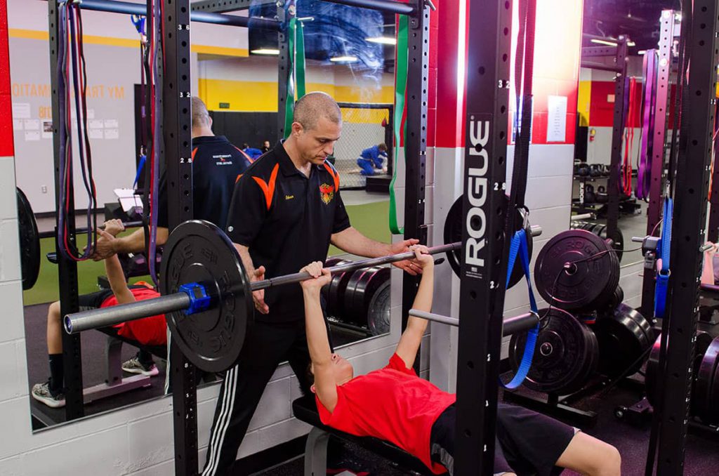 Trainer Ethan spotting a teen on the weight bench.